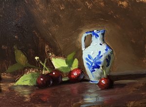 Still life oil painting of a white Delft-style pitcher with blue floral design, surrounded by ripe red cherries and green leaves on a dark wood surface.