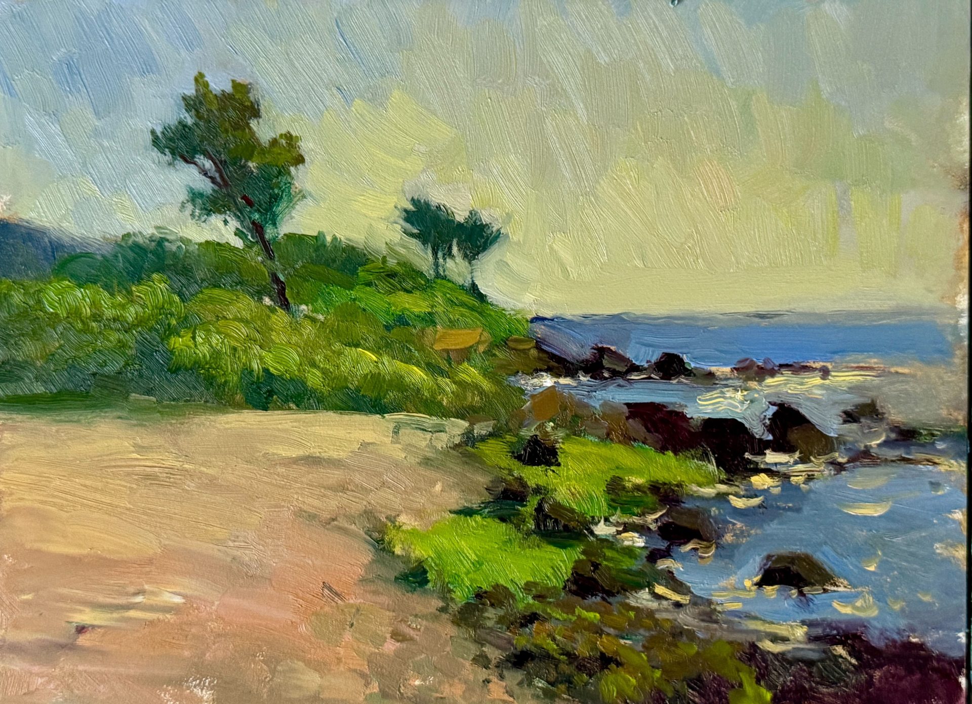 Coastal landscape oil painting featuring a rocky shoreline, vibrant green bushes, and a calm ocean under a pale, lightly clouded sky.