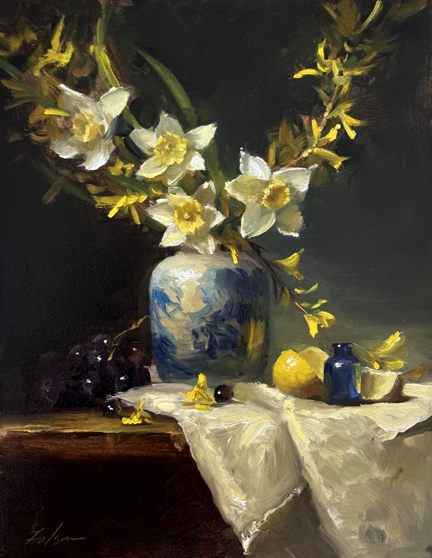 Impressionist still life oil painting of white and yellow spring flowers in a blue vase with grapes, lemon, and soft draped fabric